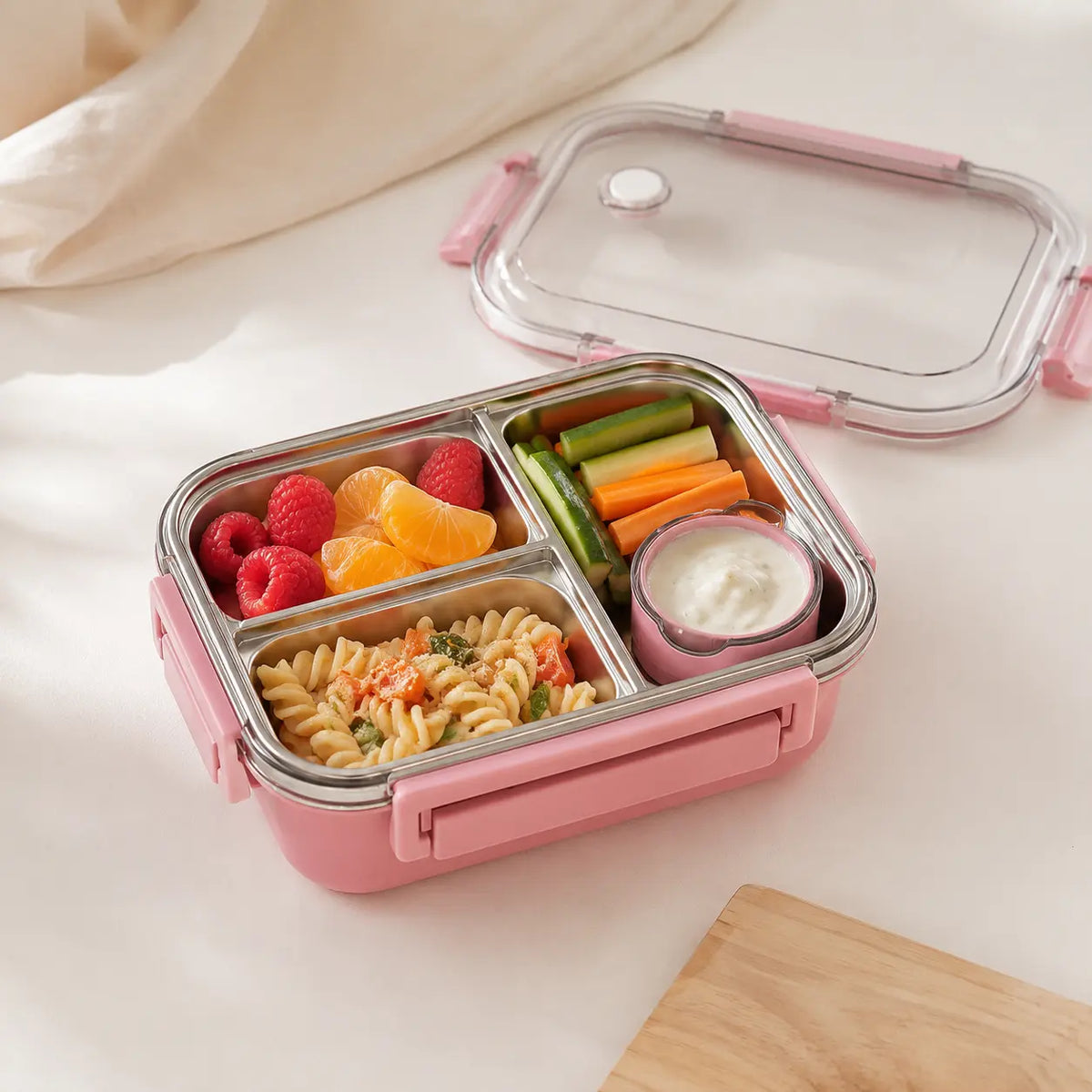 Lunch box bento rose vue de près avec trois compartiments en inox contenant différents aliments séparés.